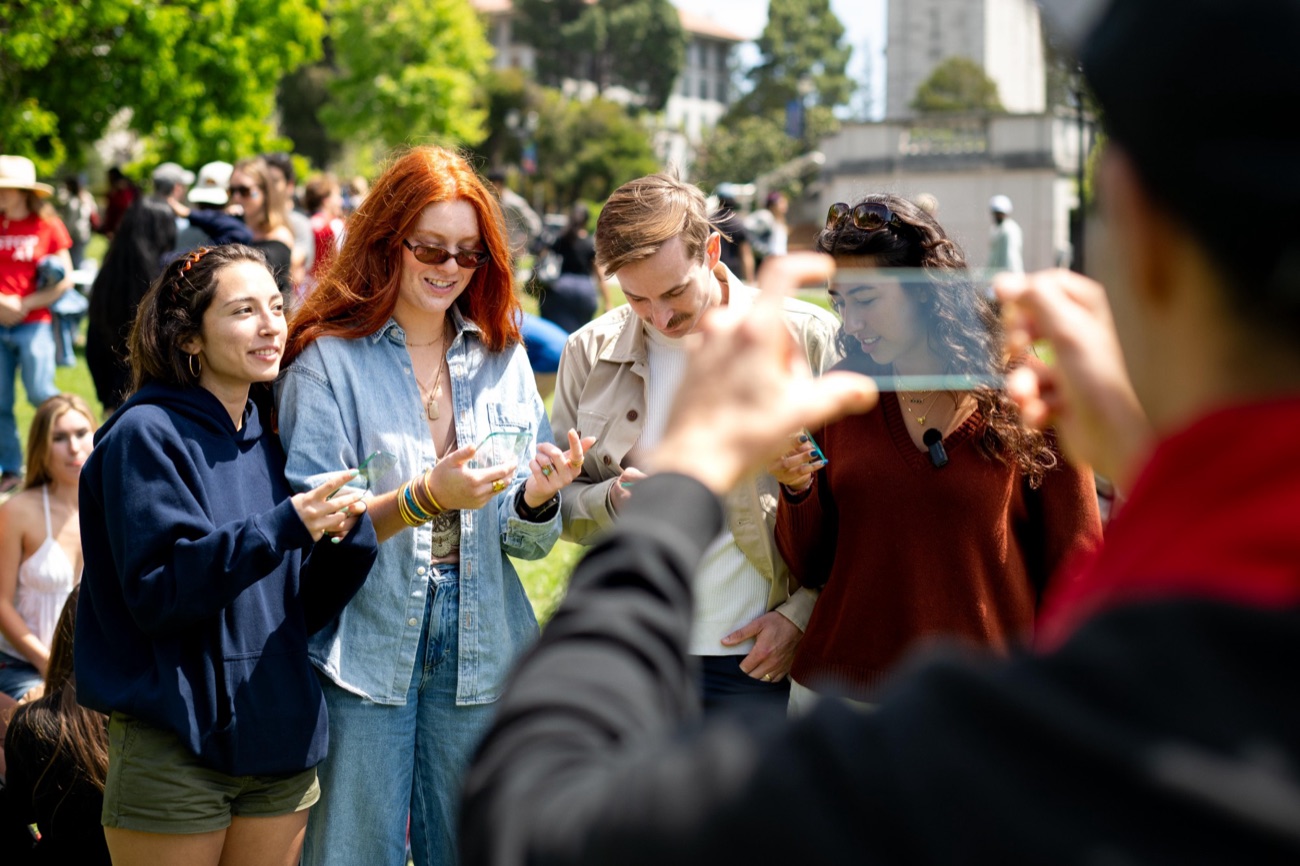 Students holding glass phone props together on the Berkeley campus, with the Campanile behind them